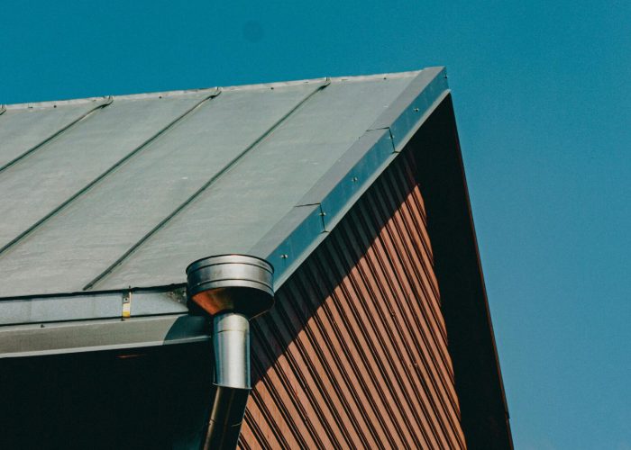 A detailed shot of a modern wooden house roof in Tartu, showcasing its steel chimney against a blue sky.